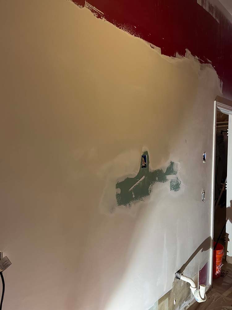 Partially painted interior wall with patch repairs, open doorway, and tools in a room under renovation