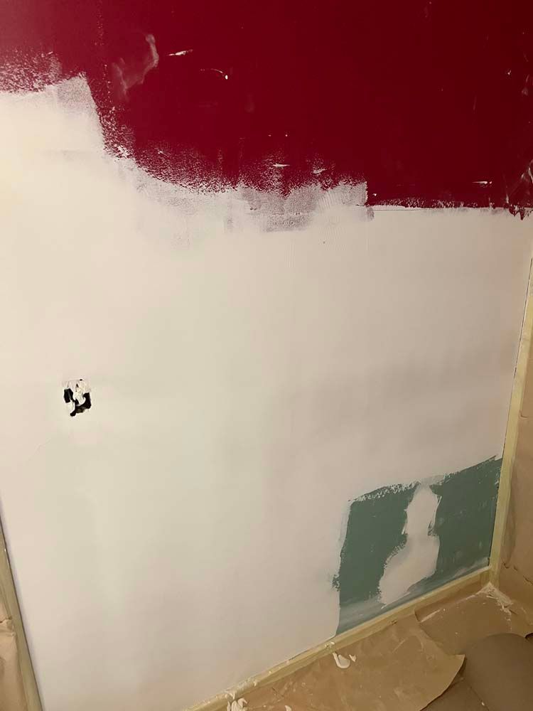 Partially painted interior wall with red upper section, white center, and green patch near the floor.