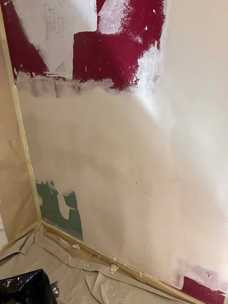 Partially painted wall with red, white, and green patches above drop cloths and masking tape