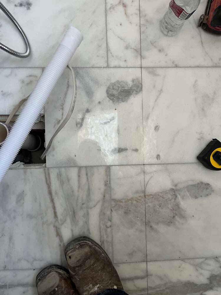 Marble floor with muddy work boots, a white hose, and a tape measure in a construction area