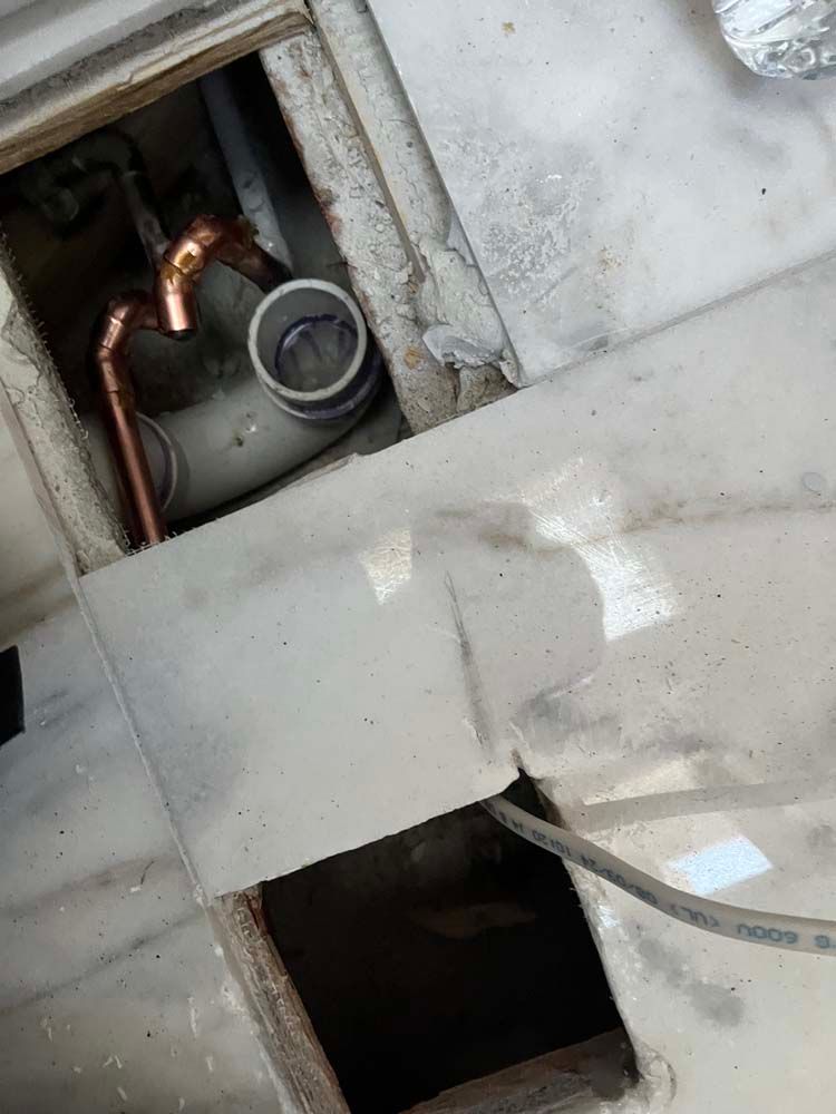 Close-up of copper pipes and a circular opening inside a white wall cavity with a dark cutout below