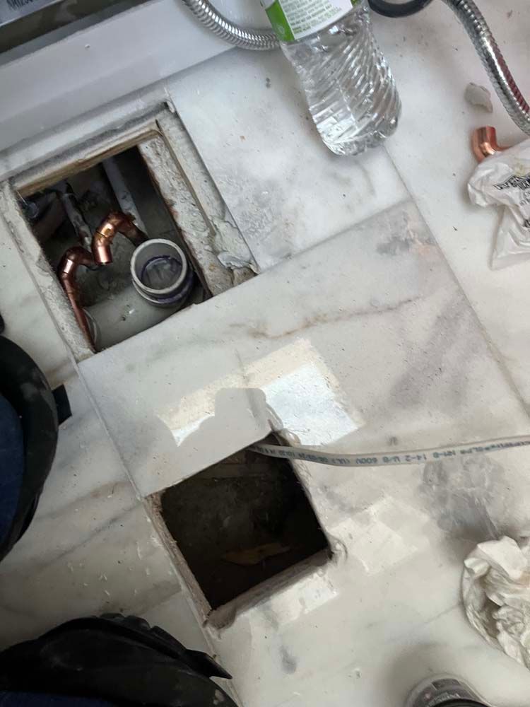 Damaged bathroom floor with two open holes exposing pipes and debris on white marble tiles