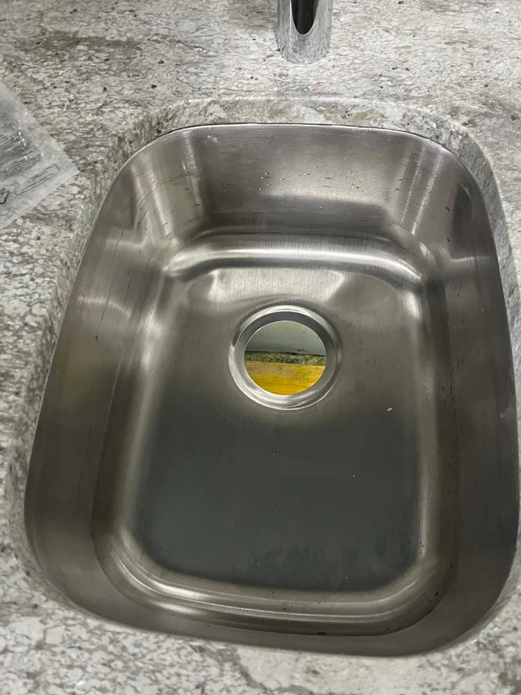 Stainless steel sink with a round drain opening and yellow residue on the bottom, set in a speckled countertop