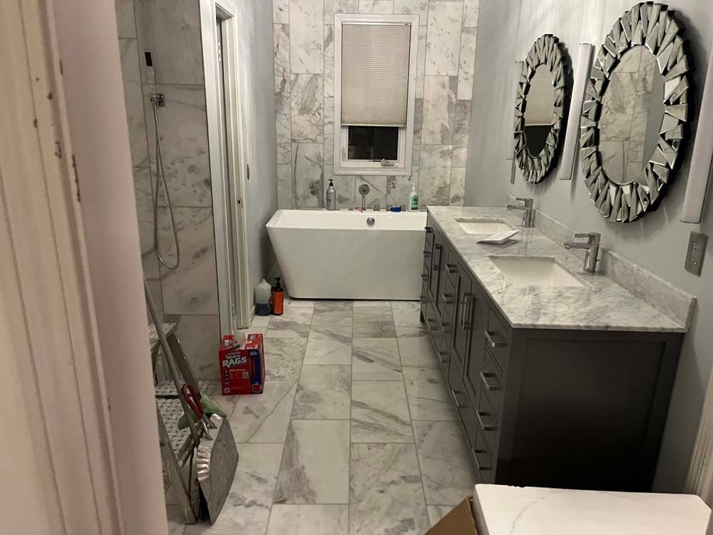 Marble bathroom with double vanity, freestanding tub, mirrors, and cleaning supplies on the floor