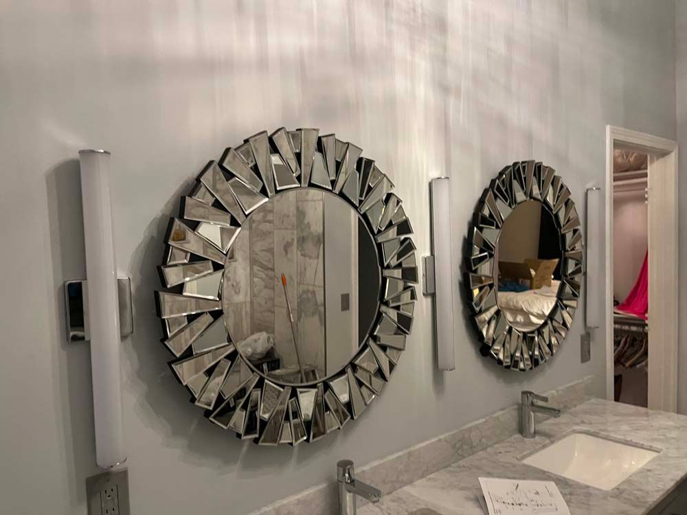 Modern bathroom vanity with two geometric mirrors, white counters, and a doorway to a pink-accented room