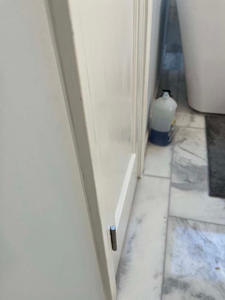 Narrow bathroom hallway with a white door, marble floor, and a gallon jug near the wall