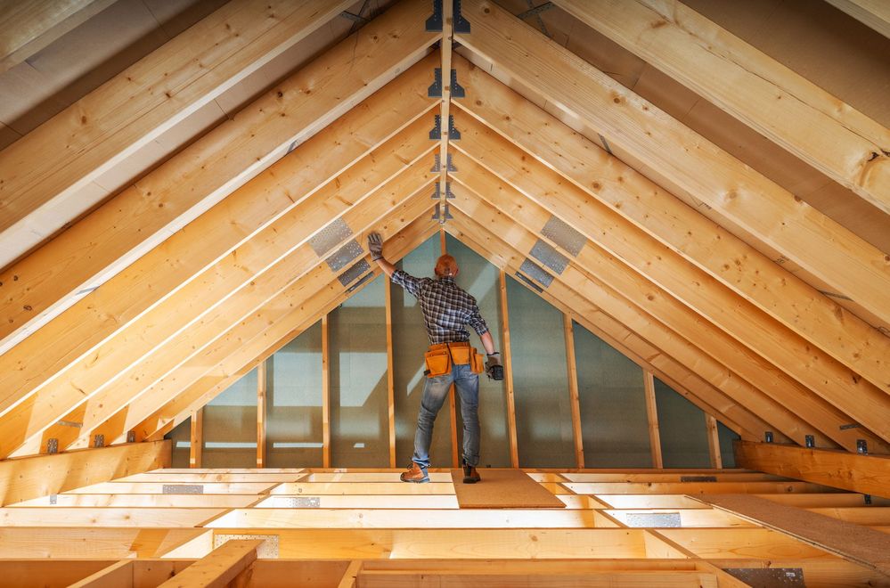 Worker installing attic insulation beneath wooden roof beams