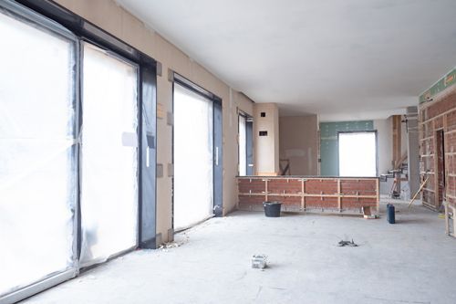 Office remodeling contractors renovating interior with exposed walls and plastic-covered windows