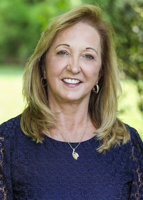 Woman smiling outdoors in a navy lace top with a green blurred background