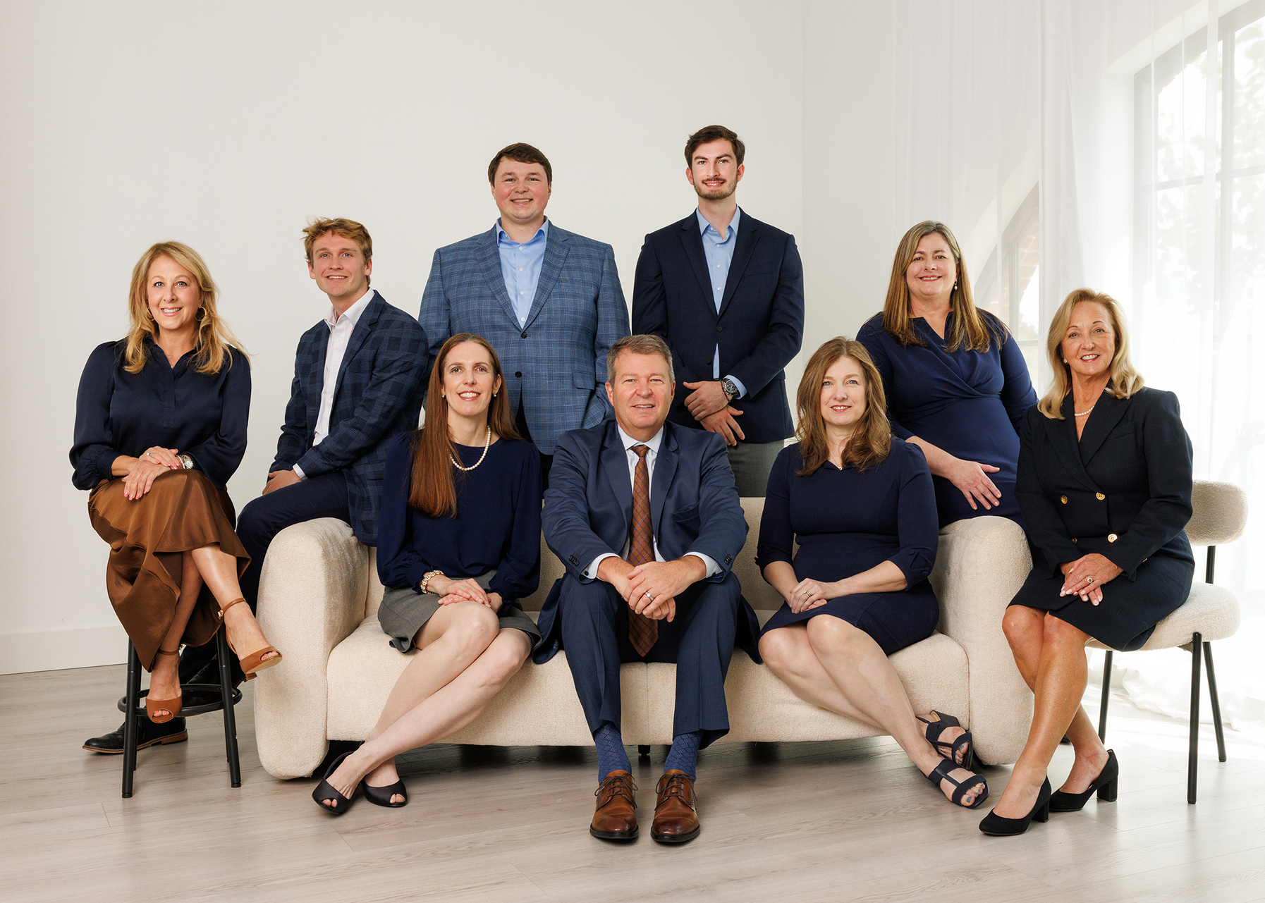 Seven people posing in a bright office lounge, seated and standing in formal attire