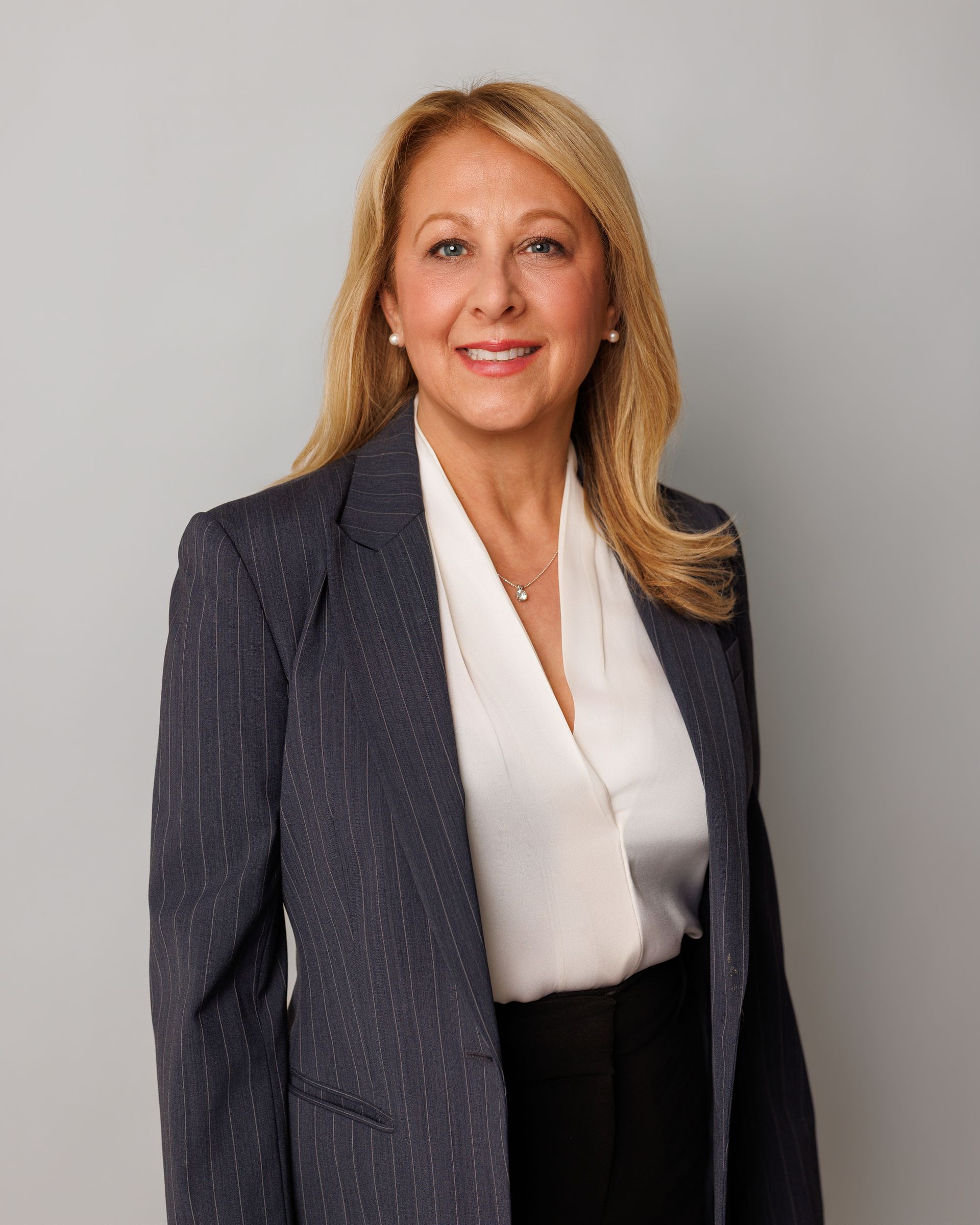 Portrait of a smiling woman in a navy blazer and white blouse against a gray backdrop