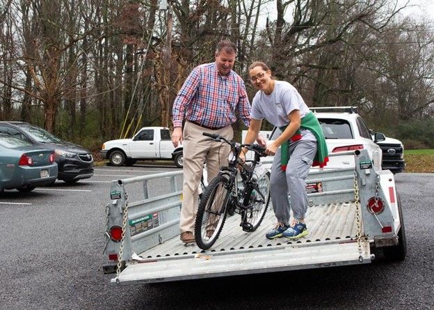 Two people loading a bicycle into a pickup truck on a wet parking lot