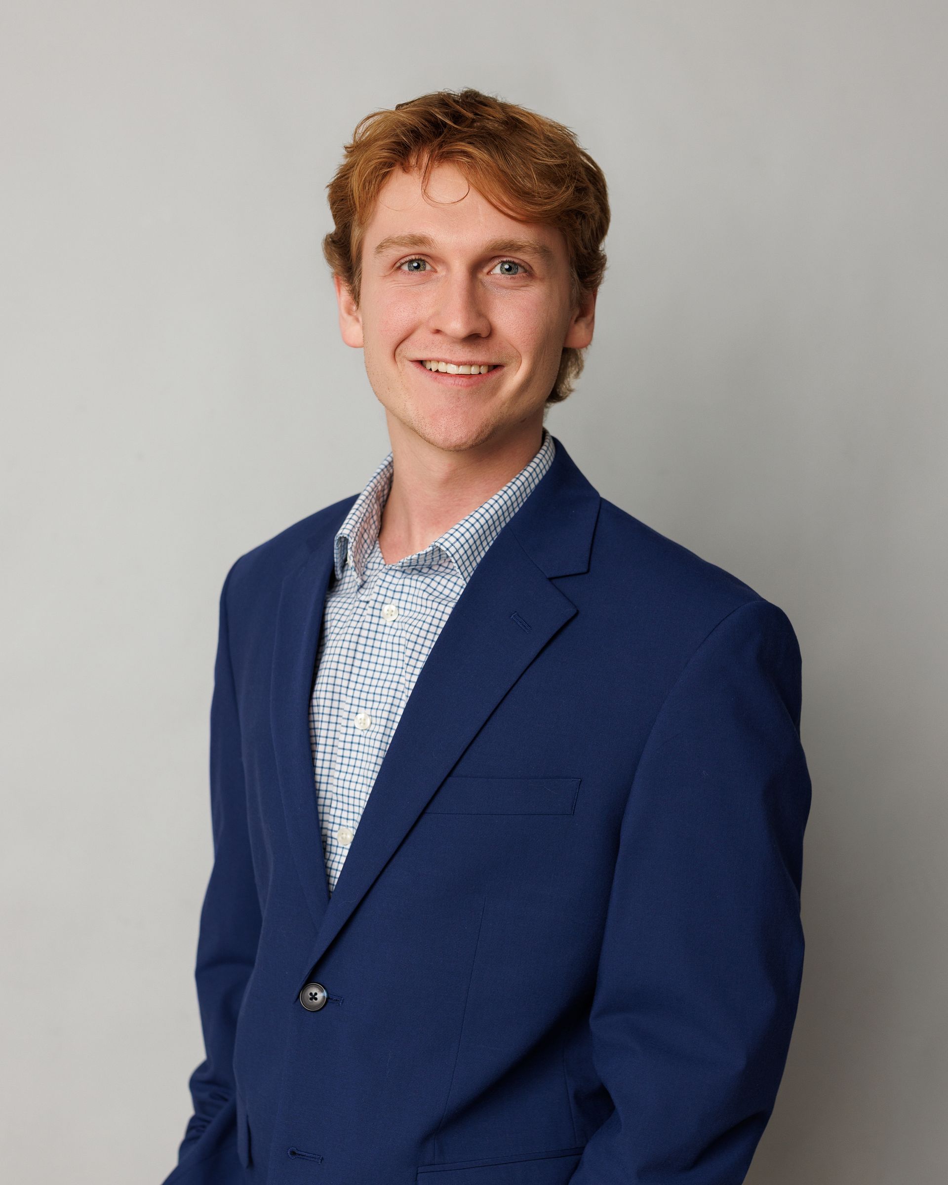 Person in a blue blazer and patterned shirt smiling against a plain gray background