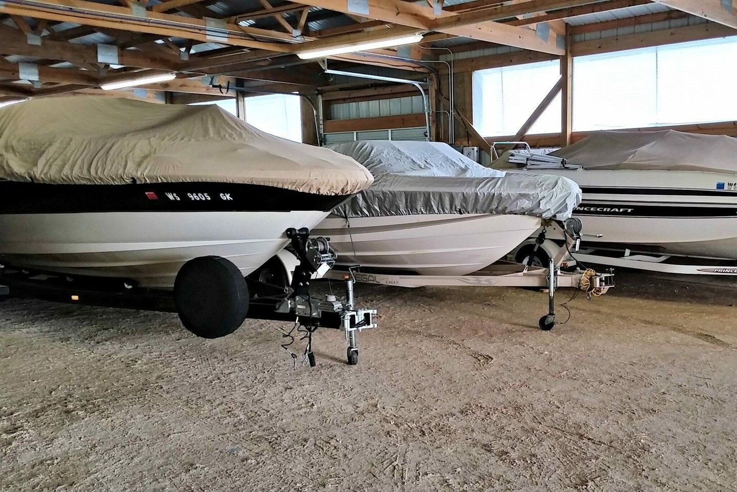 Covered boats stored in a wooden boathouse on trailers over gravel floor