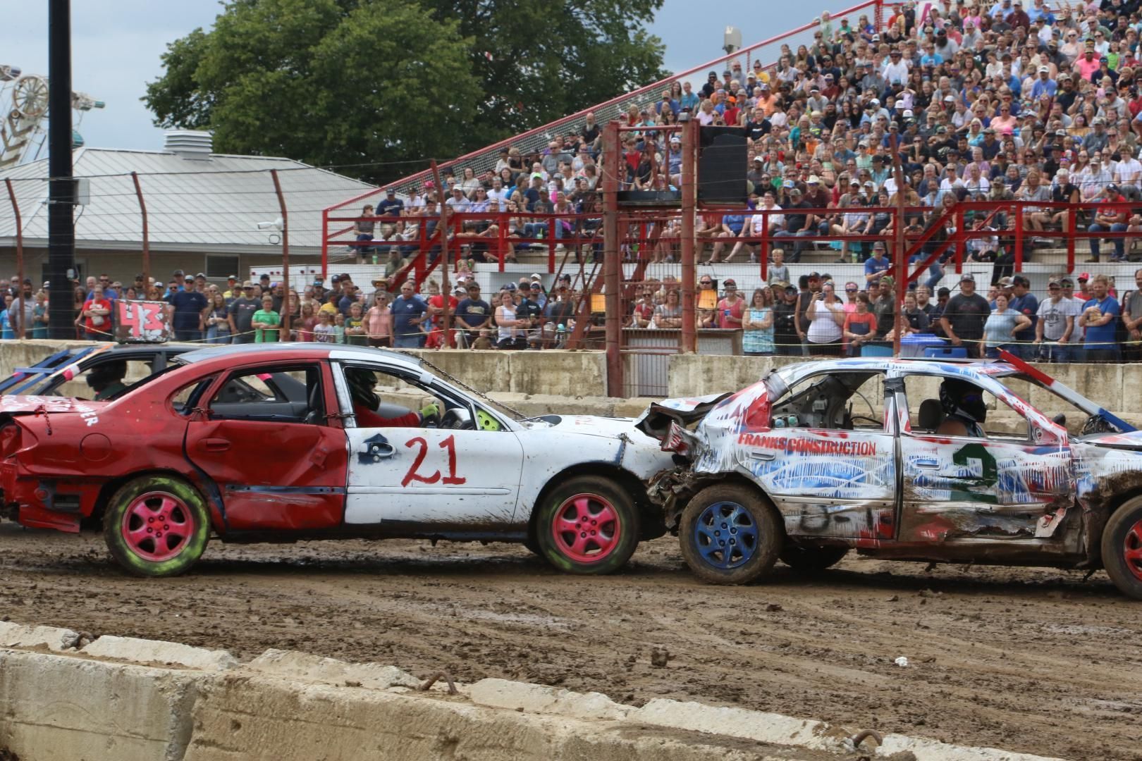 Two damaged race cars collide on a muddy track in front of a packed grandstand.