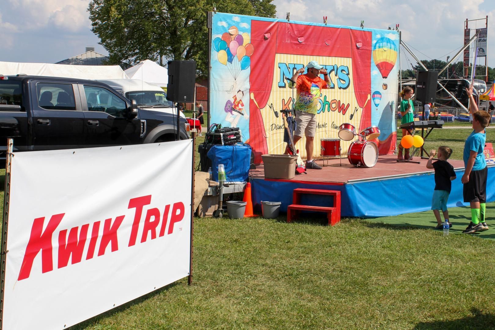 Kwik Trip booth at an outdoor festival with colorful stage and people nearby