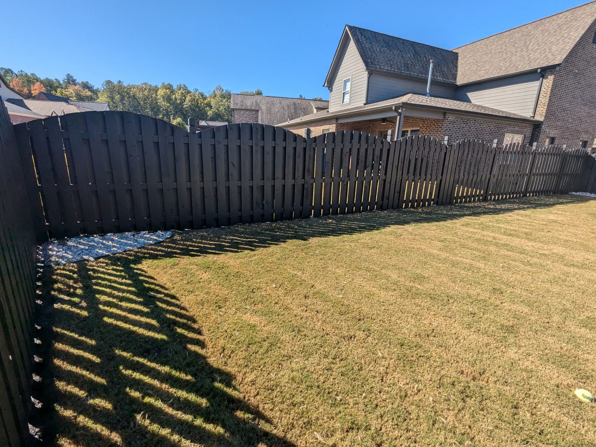 A wooden fence surrounds a lush green lawn in front of a house.