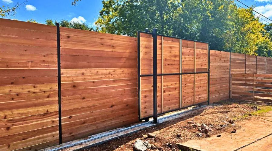 Modern horizontal wood privacy fence featuring a large sliding gate and black metal posts, representing a professional full fence replacement.