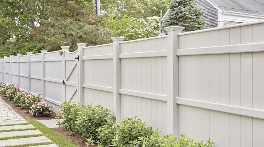 Professional installation of a white privacy fence and matching gate alongside a landscaped residential walkway.