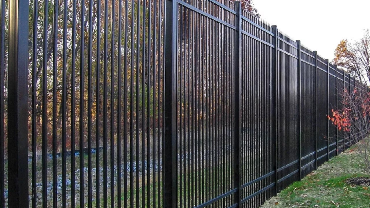 Black metal security fence along a grassy slope, with trees in the background.
