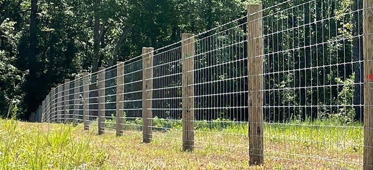 A fence made of wire and wooden posts in a grassy field.