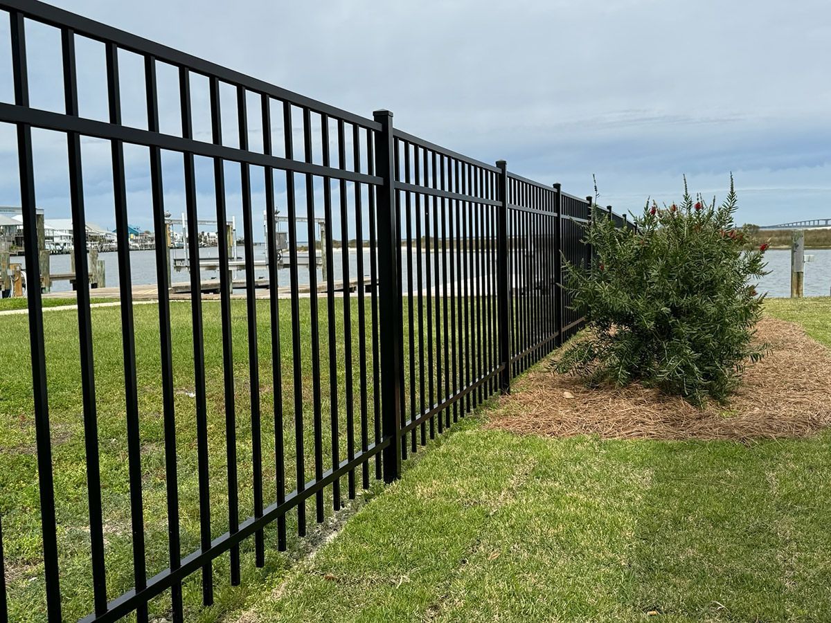 A black metal fence surrounds a grassy area next to a body of water.