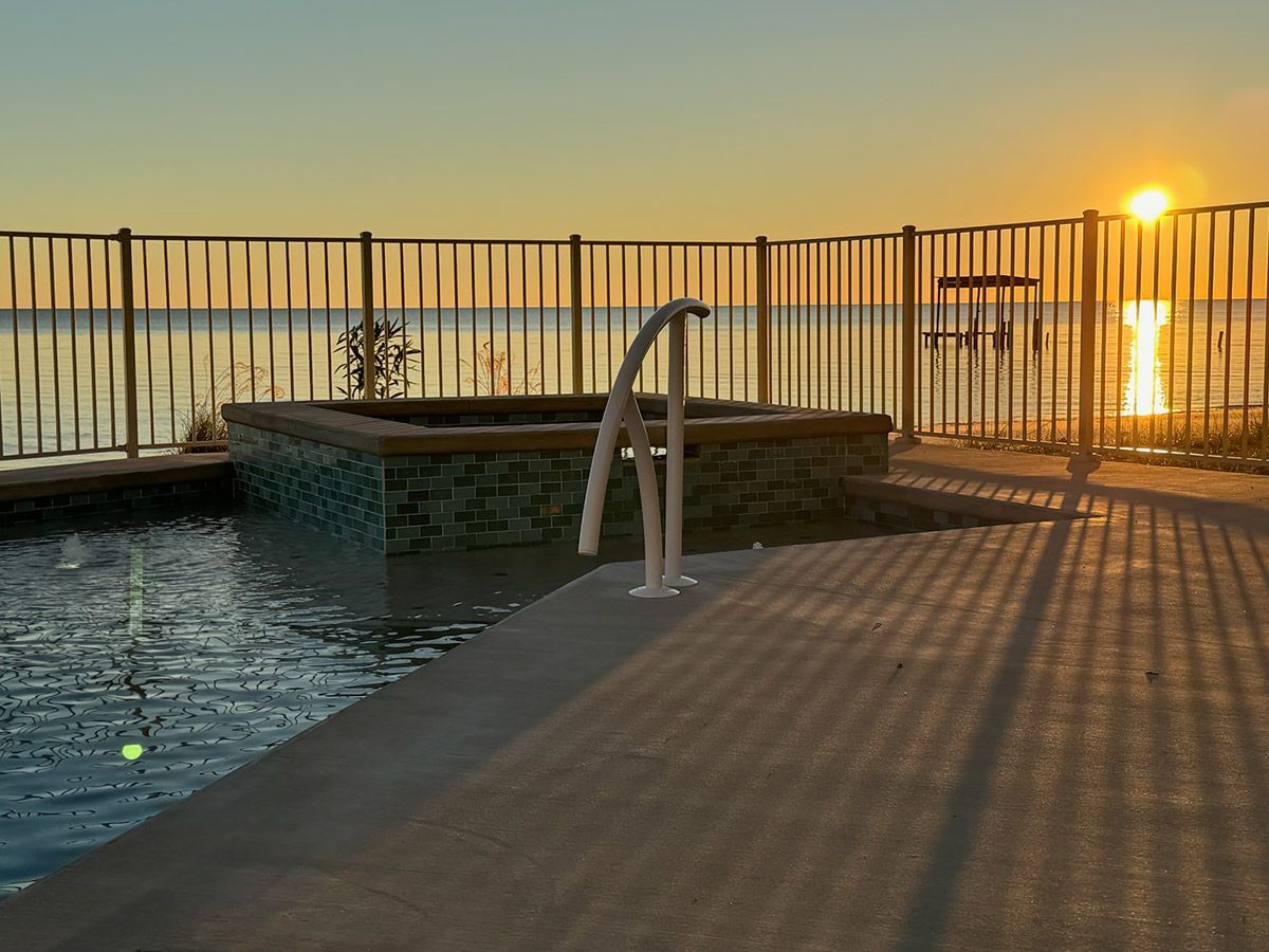 A swimming pool surrounded by a fence with the sun setting in the background