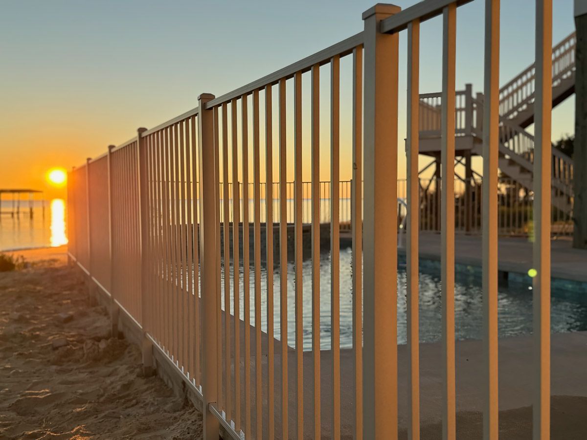 A metal fence surrounds a swimming pool at sunset.