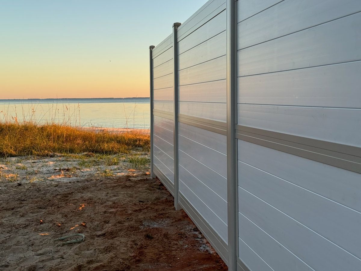 A white fence surrounds a beach with a view of the ocean.
