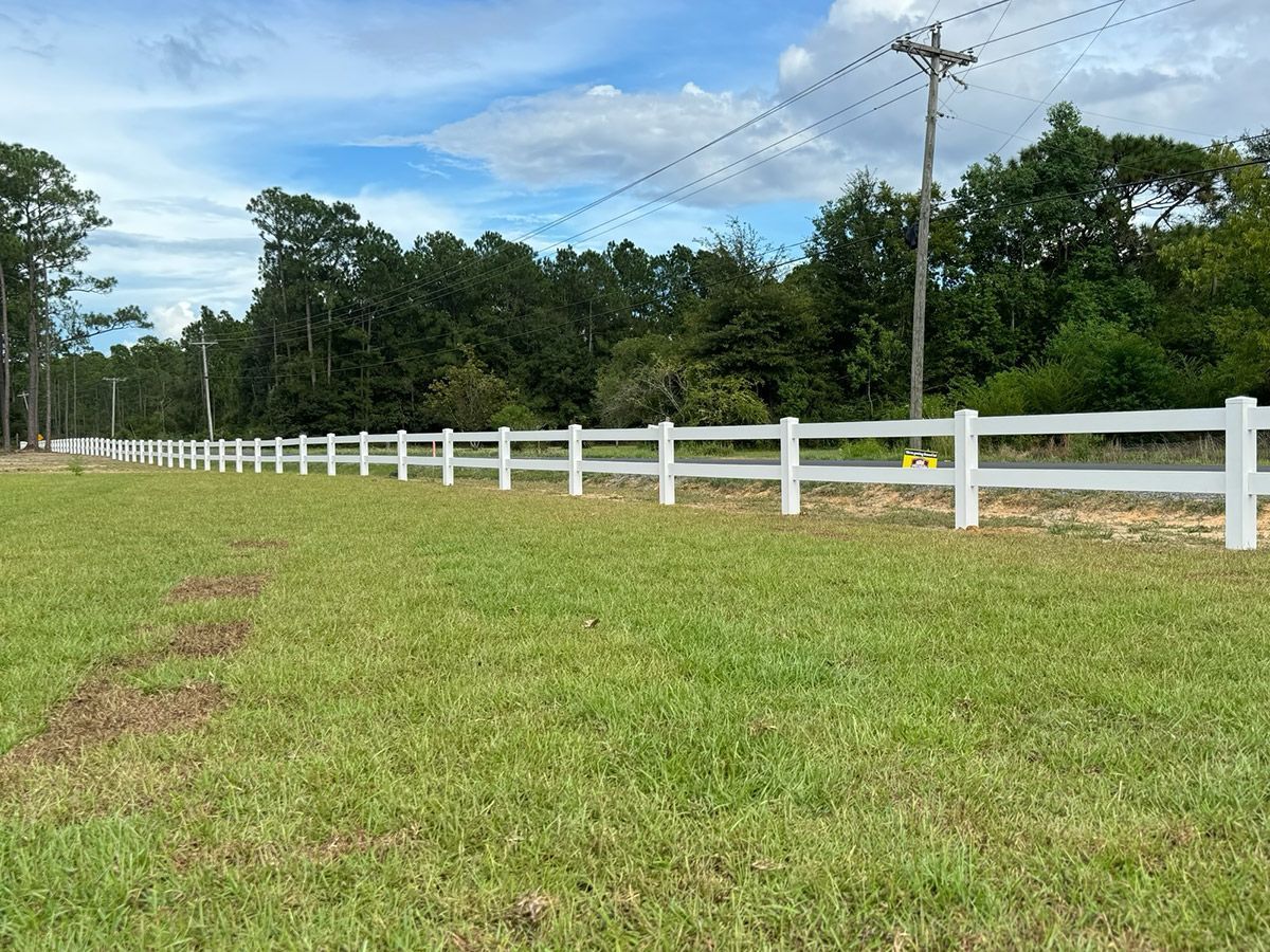 A white fence surrounds a grassy field with trees in the background.