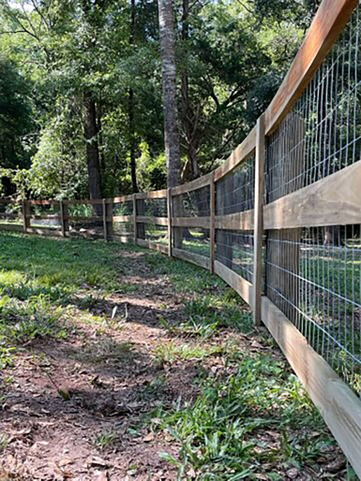 A wooden fence with a wire fence surrounding a grassy field.
