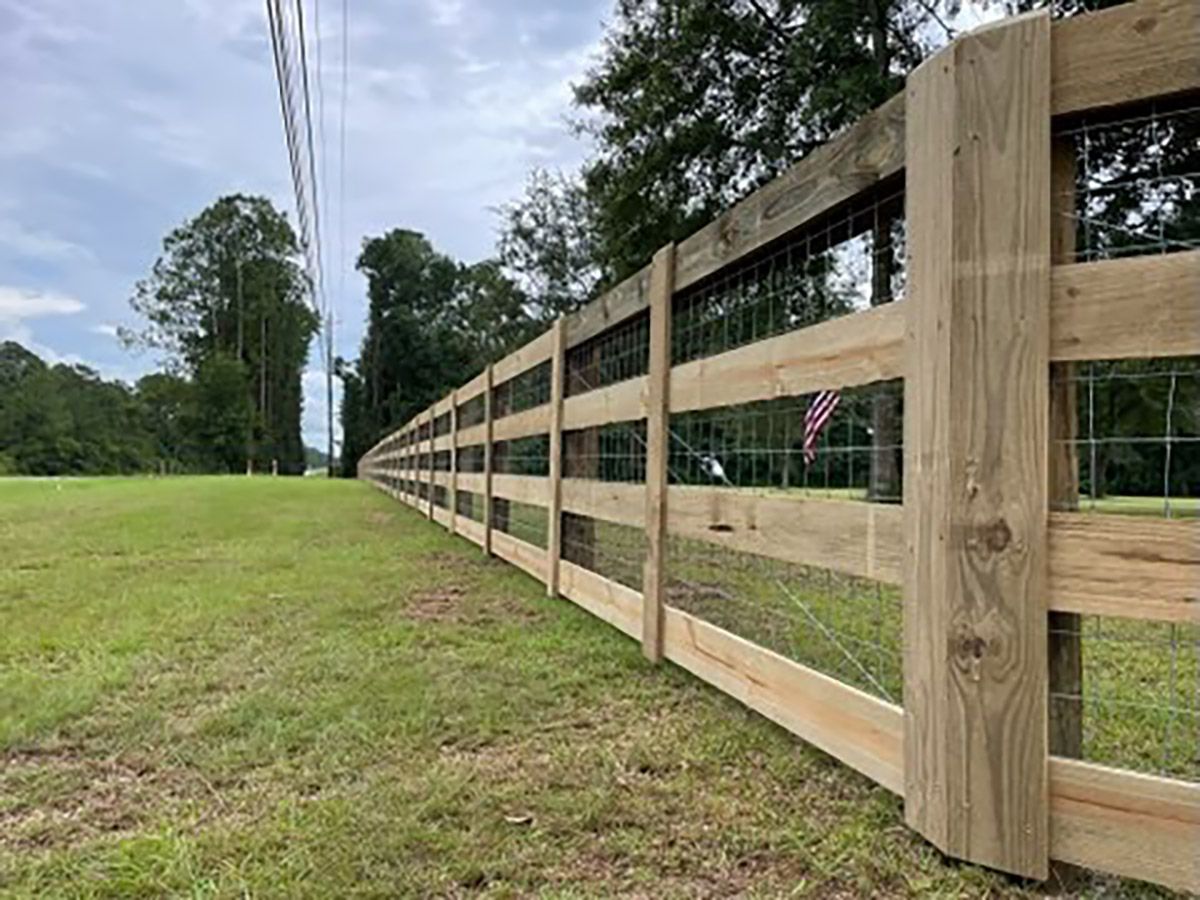 A wooden fence surrounds a grassy field with trees in the background.