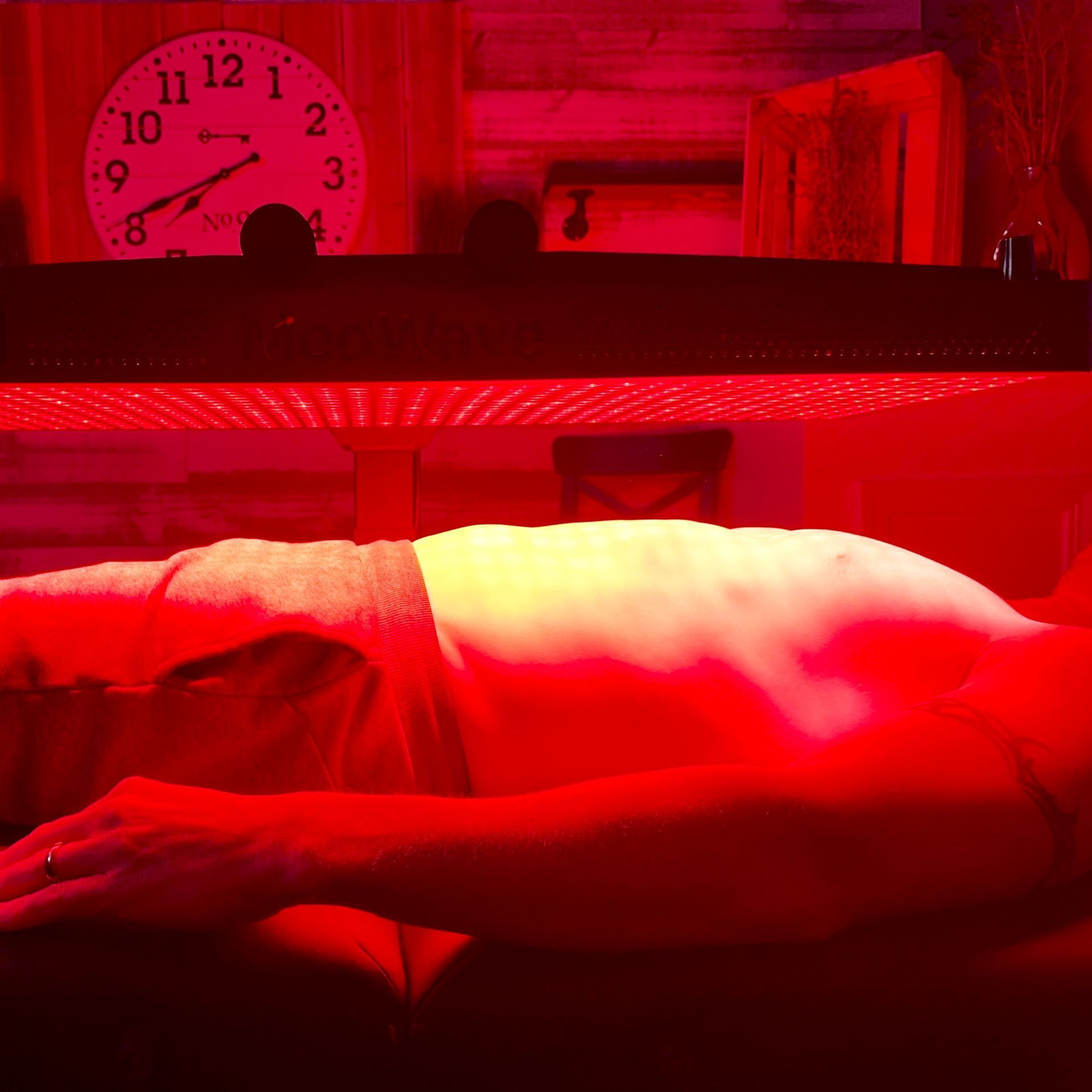 Person receiving red light therapy on their abdomen. Red light illuminates the body.