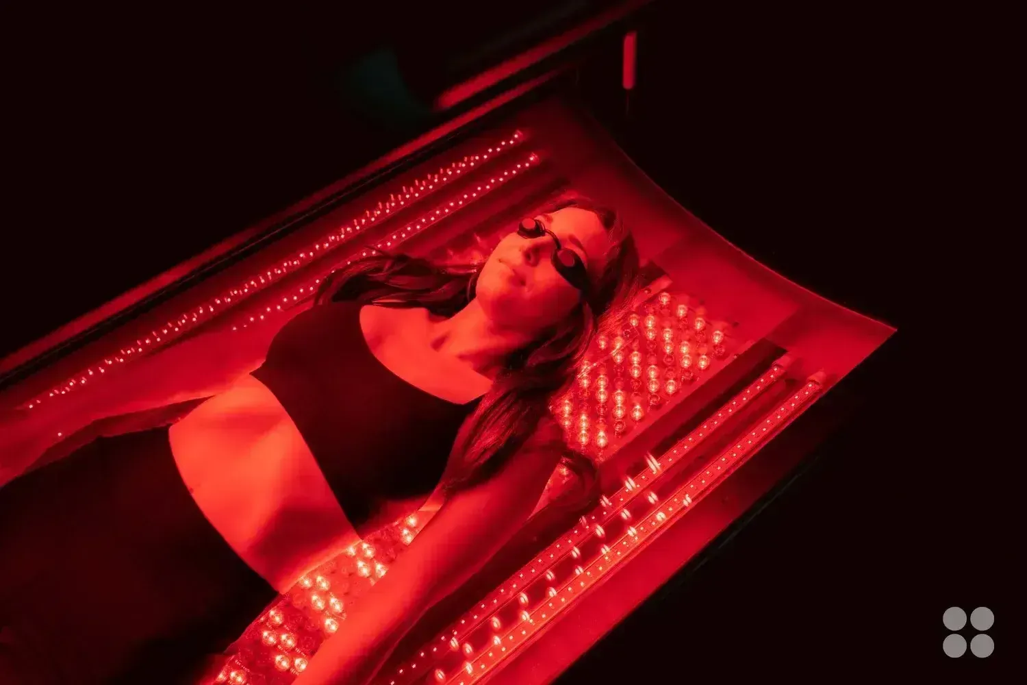 Woman wearing eye protection lies on a red light therapy bed.