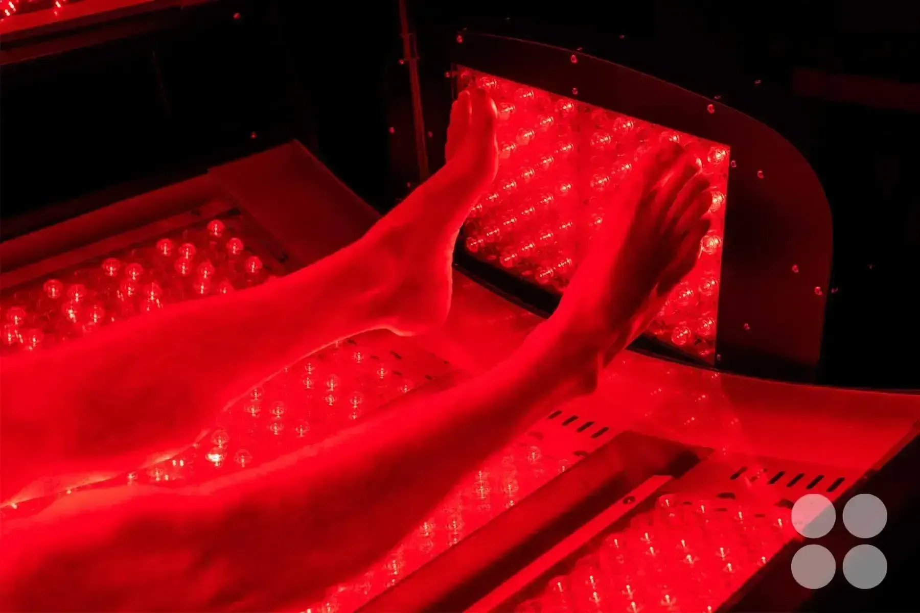 Feet inside a red light therapy device, emitting a red glow.