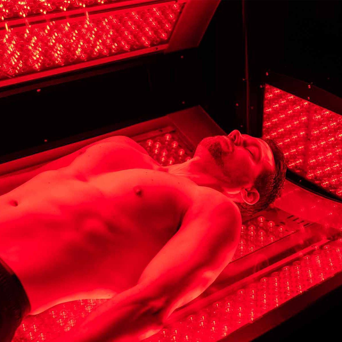Man lying under red light therapy panels.
