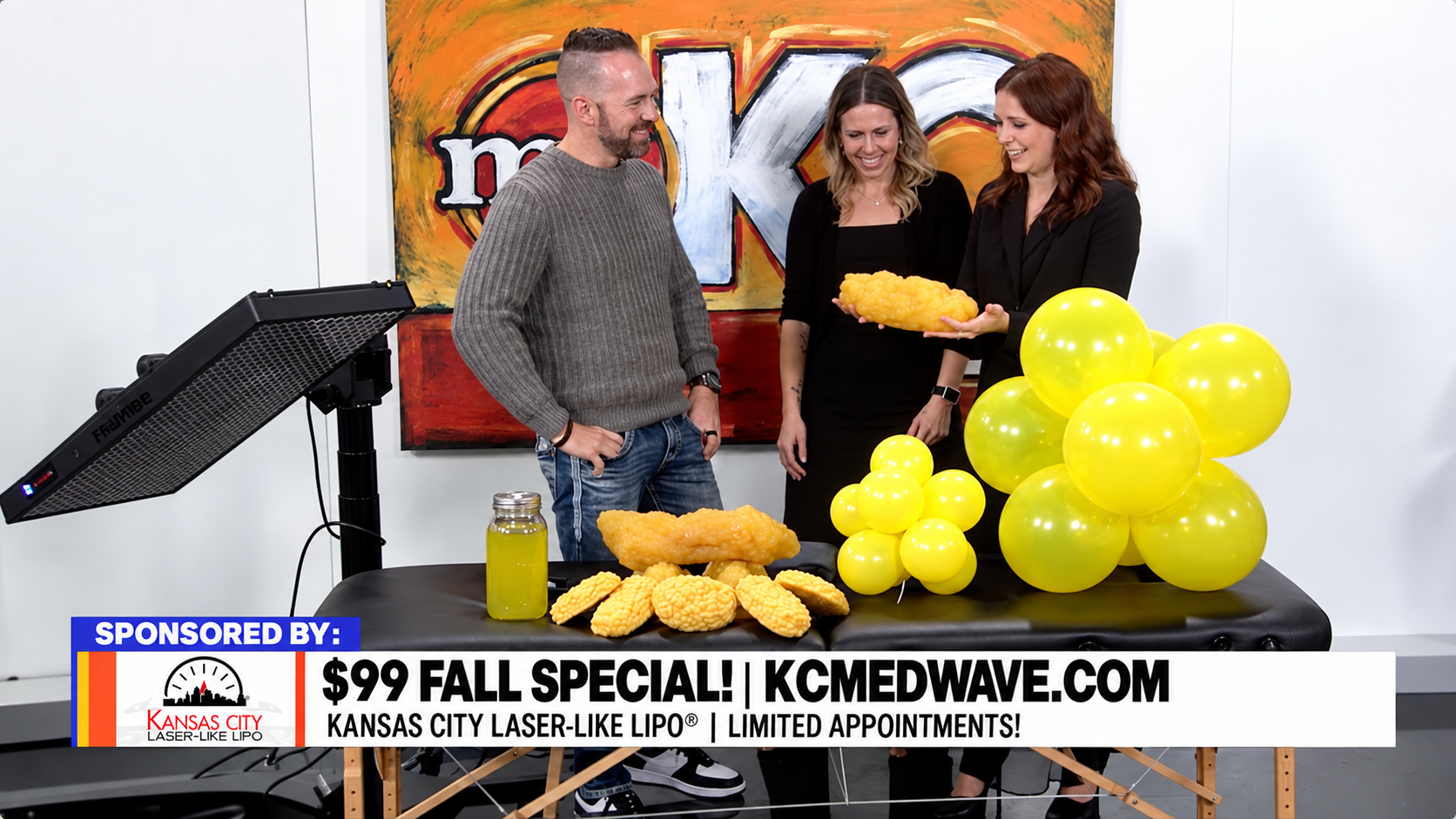 Three people at a studio with yellow balloons, standing beside a sign for a $99 fall special.
