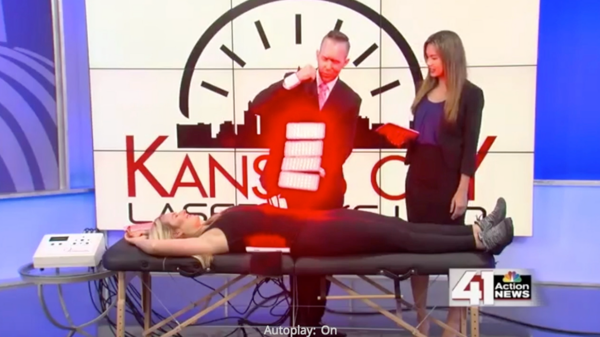 A man demonstrates laser therapy on a woman lying on a table in a studio with a cityscape graphic.