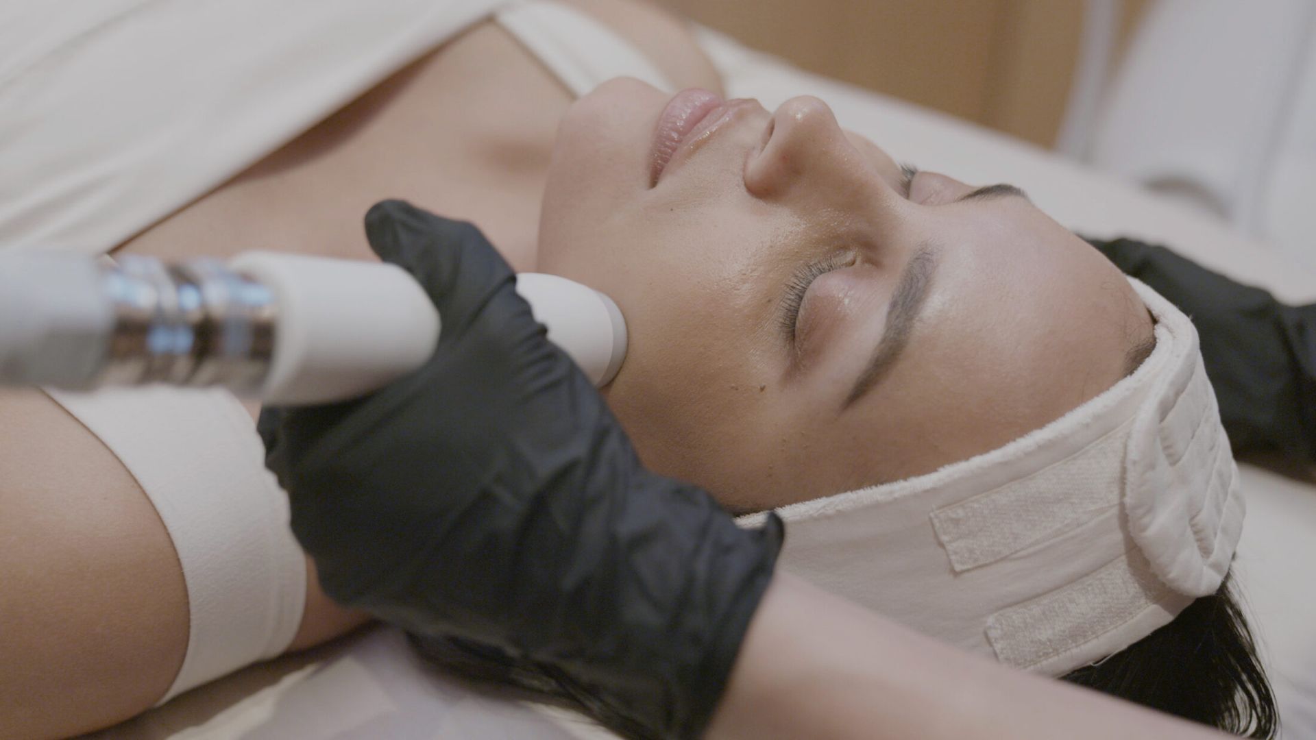 Person receiving a facial session with a gloved hand using a Artemis T-Shape 2 handheld device on the face