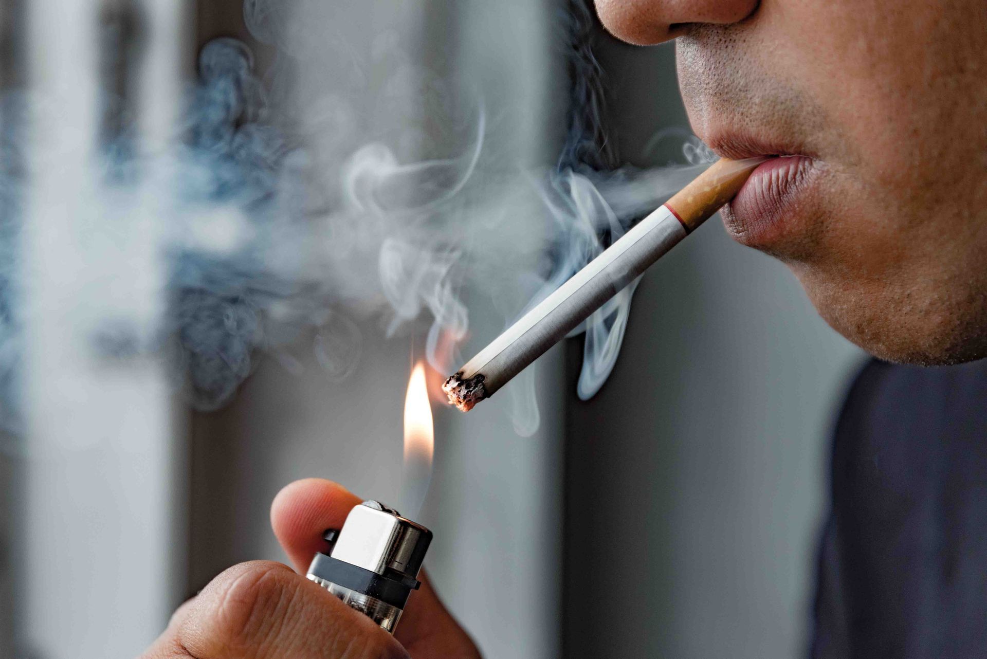 Person lights a cigarette, smoke rising, indoors.