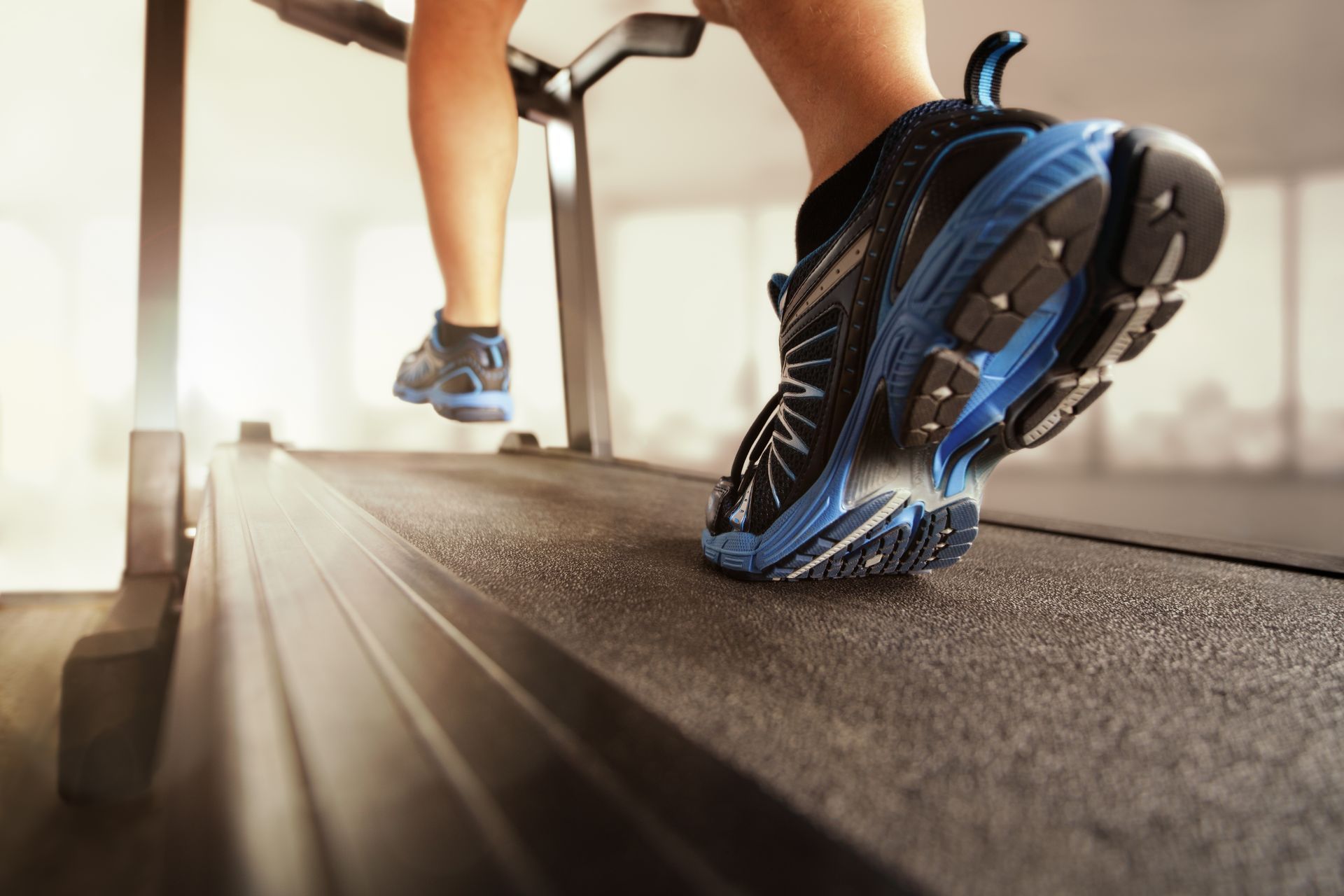 Person running on a treadmill; black and blue running shoes visible.