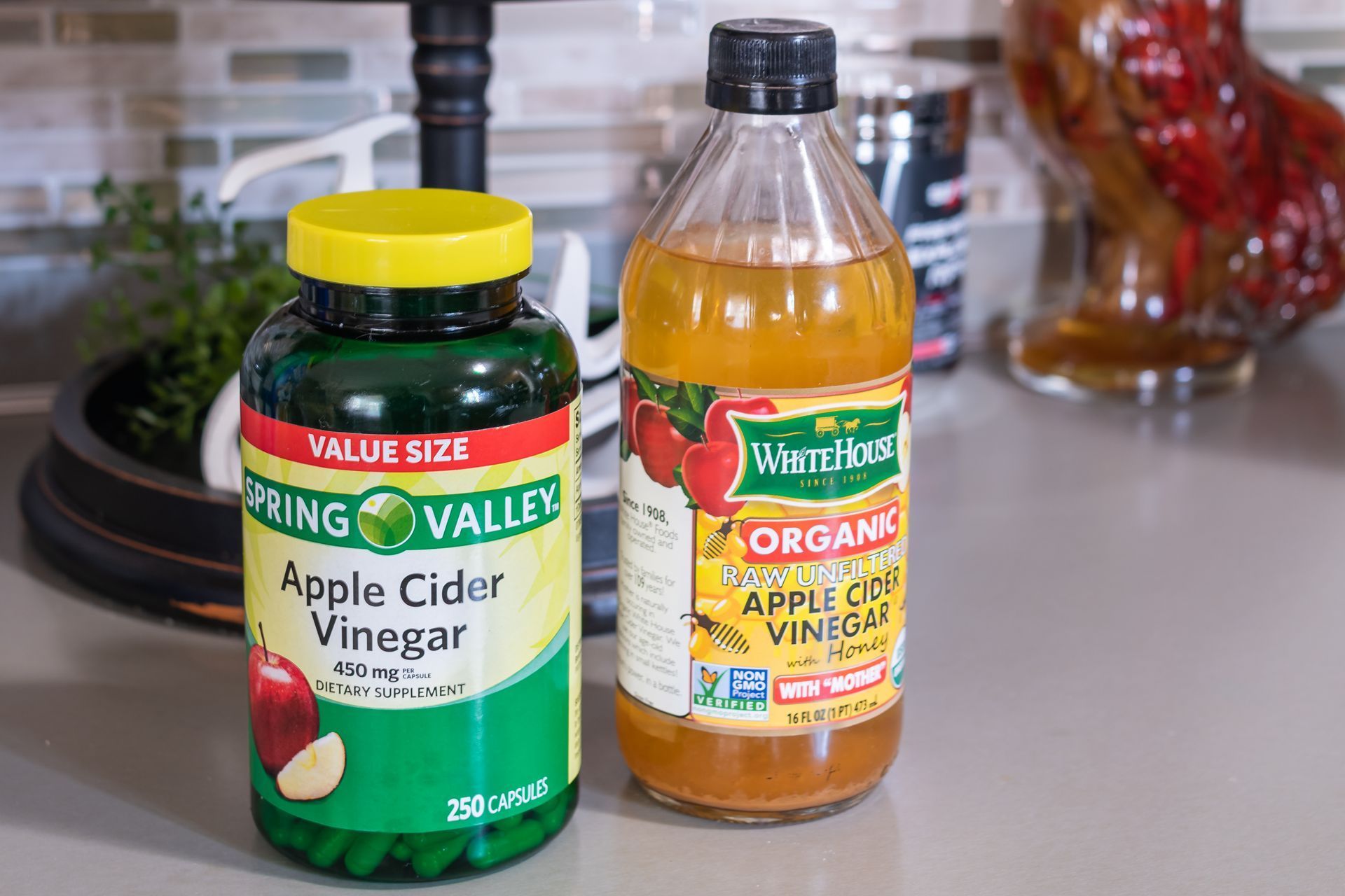 Two bottles of apple cider vinegar, one green and yellow, one clear and orange, on a countertop.