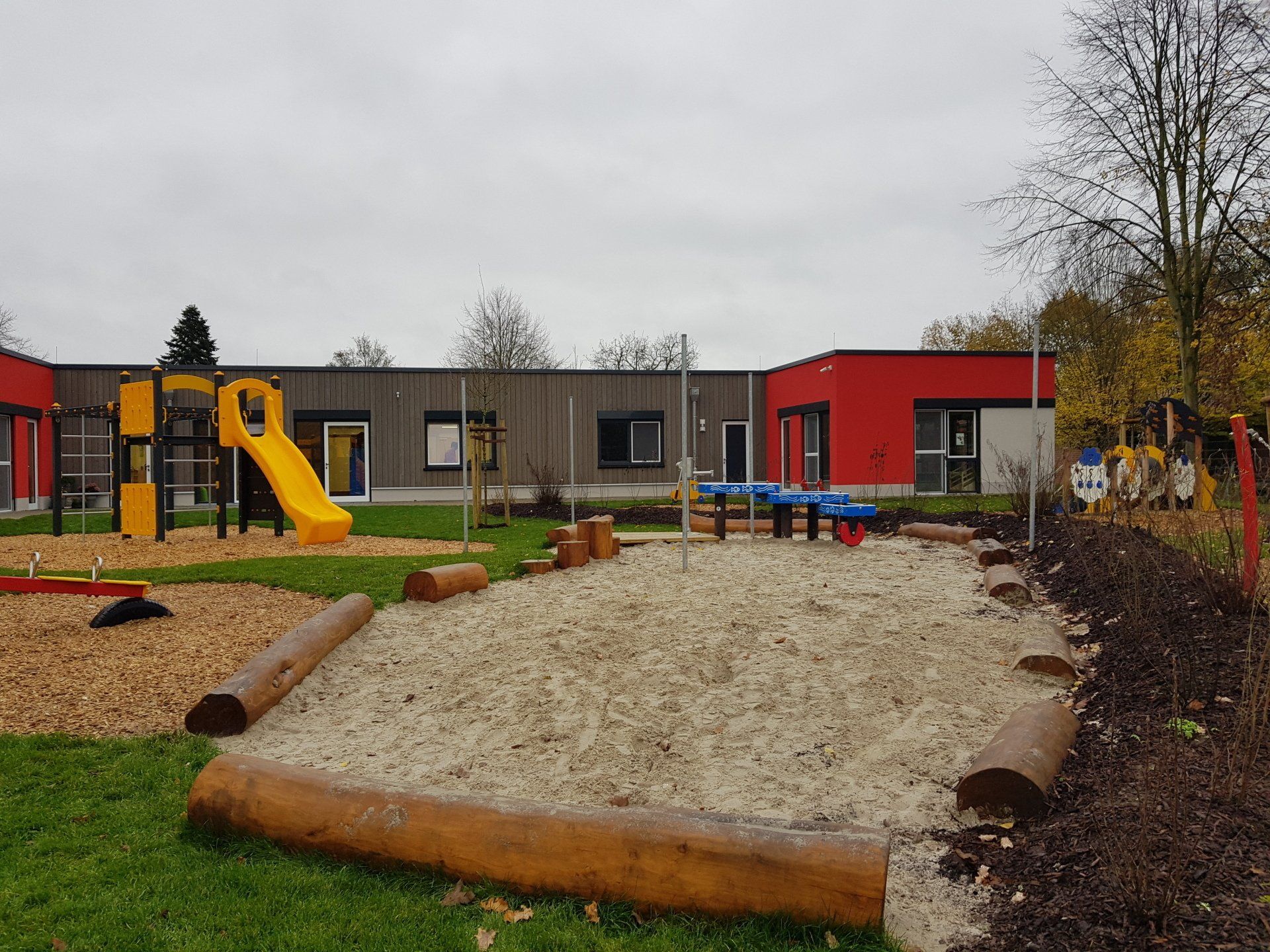 Ein Spielplatz mit Rutsche und Sandkasten vor einem Gebäude.