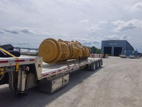 Yellow industrial machinery is loaded on a flatbed truck outdoors on a cloudy day.