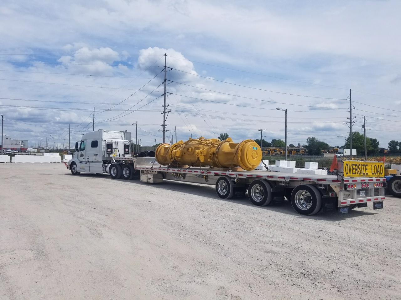 A semi-truck carrying a large yellow industrial component on a flatbed trailer, outdoors.