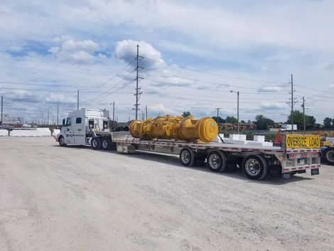 A semi-truck carrying a large yellow industrial component on a flatbed trailer, outdoors.