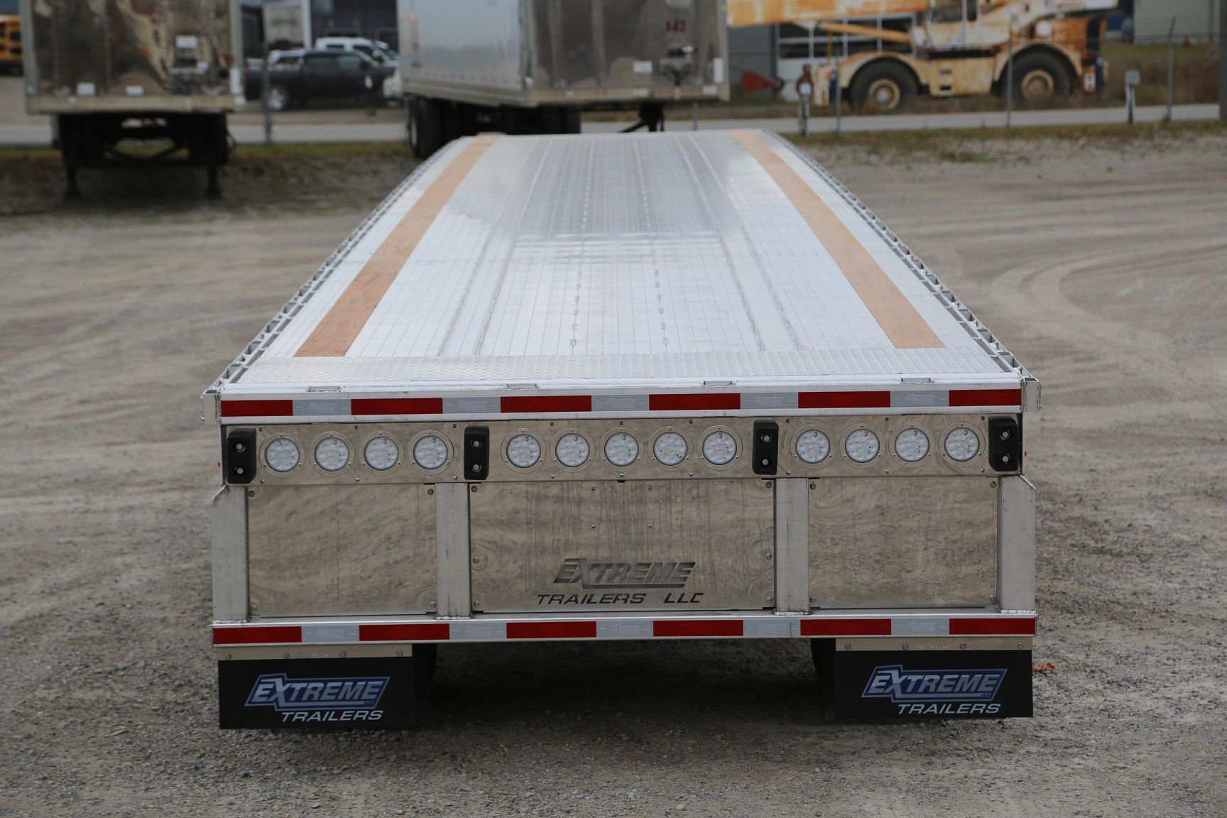 Rear view of a silver flatbed trailer with orange and red stripes, parked outdoors.