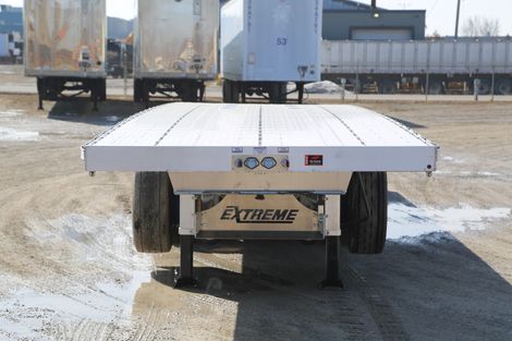 A white flatbed trailer with a black undercarriage is parked outdoors on a sunny day.