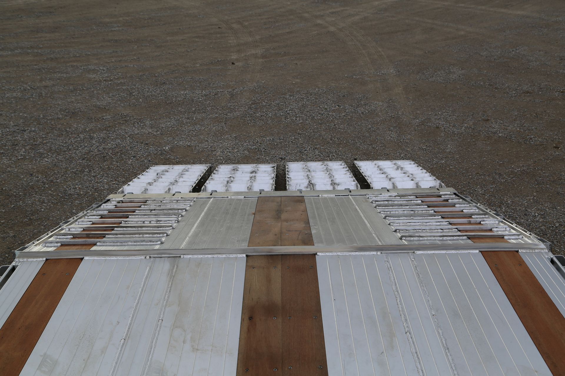 Overhead view of a trailer bed with wooden planks and metal, parked on a gravel surface.