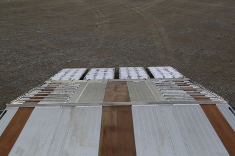 Overhead view of a trailer bed with wooden planks and metal, parked on a gravel surface.